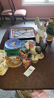 Photo of assorted chicken themed kitchen items on table, including trays, figurines, and oven mitts.
