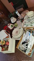 Top view of Christmas plates, bowls, green glass bowls, and holiday candles on table with assorted seasonal decor items.