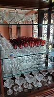 Glass cabinet shelves with multiple clear etched and red drinking glasses and dessert bowls