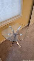 Full view of a round glass top side table showing clear glass and metal base with curved legs.