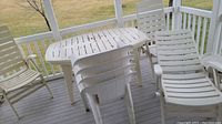 Photo showing entire outdoor table with six white plastic chairs and one lounge chair around it on a deck.