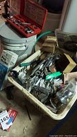 Overview of assorted hand tools including socket set on top of paint bucket and basket with various tools and hardware.