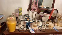Candles and various candle holders including brass and glass, star-shaped holders, votive candles, and a large yellow jar candle on a table with a mirror and decorative items.