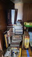 Photo showing a stack of DVDs and CDs. Deadwood The Complete First Season box set and multiple CDs and DVDs visible in shelf space.