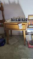 Front view of mid century modern wooden side table with chess set on top. Shows the single drawer front panel and tapered legs.