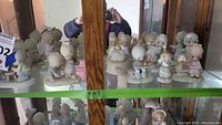 Photo of multiple Precious Moments figurines displayed inside a glass cabinet shelf with reflections showing. Figurines include children and an angel, all with pastel colors and detailed bases.