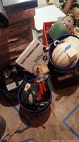 Buckets and bins on floor full of assorted tools, a roll of soft copper tubing, and hard hats visible with original boxes and wire.