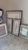 Six framed art prints leaning against wall in a corner, showing varying sizes and styles including floral and embossed seashell art