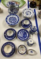 Overview photo showing various blue and white china items including plates, cups, saucers, a creamer, and a small covered container arranged on a table.