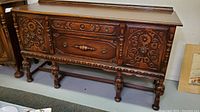 Front view of wood buffet cabinet showing carved doors, drawers, and turned legs