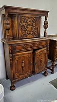 Full view of wooden Spanish Revival style hutch cabinet with detailed carvings on upper and lower doors, two-door lower cabinet, and drawer.