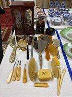 Full overview of the lot on a table showing jewelry boxes, vintage grooming brushes and mirrors, and assorted plates in background.