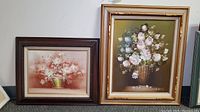 Two framed floral oil paintings shown together, one with dark brown frame and one with gold frame, both signed.