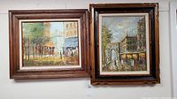 Two framed original oil paintings side by side on a wall showing different city scenes.