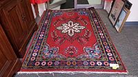 Full view of the vintage Persian rug showing the central floral medallion, detailed blue and black borders, and the right edge with noticeable wear and fraying.