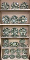 Various sizes of green and yellow rooster motif porcelain plates and a matching bowl arranged on shelves