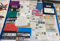 Photo showing a variety of postage stamps on album pages, multiple First Day cover envelopes, vintage correspondence, and stamp passport books spread out on a surface.