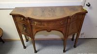 Front view of sideboard showing three drawers, two cabinets, serpentine front and brass hardware