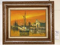 Full view of the framed nautical painting showing boats at a dock during sunset with vivid orange sky and reflection in the water. The painting is held in a carved wooden frame with cream liner.