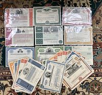 Top view of various stock certificates laid out, showing multiple different company names and certificate colors and designs.