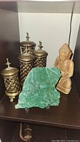 Image showing the four brass candle holders with cut-out lattice design, the green jade slab, and the carved wooden Buddha figure together on a shelf