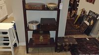 Shelf displaying the Amish aluminum bowl, three chest-type wooden boxes, a wooden inlay box and an enameled brass plate with peacock.