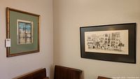Room corner showing both framed prints hung on the walls above two chairs. One print is black and white architectural facade; the other is a colored door with green mat.