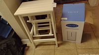Humidifier boxed and white folding kitchen stool placed on tile floor.
