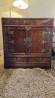 Front view of wooden Korean chest showing five small drawers, two doors with brass hardware, detailed wood grain, and damage on one door.