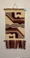 Handwoven yak wool wall hanging with geometric design in earth tones, hung on a wall.