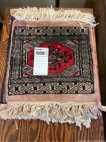 Four handwoven Pakistani table mats stacked on a wooden surface showing varying traditional geometric patterns and cream fringes