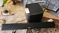 Black Polk Audio soundbar positioned in front of cube subwoofer on carpet.