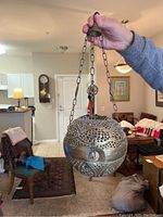 Full view of the brass sacristy lamp suspended by chains being held in hand showing overall shape and finish