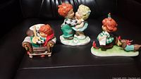 Three Goebel figurines displayed together on dark leather surface showing entire group