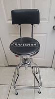 Front view of Craftsman hydraulic stool showing black cushioned seat with logo and backrest