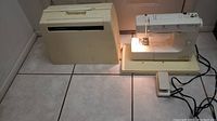 Full view of Kenmore 7 sewing machine with case and foot pedal on tiled floor, corded and plugged in light on showing functionality.