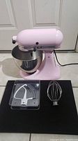 Front view of pink stand mixer with bowl and two attachments on display board