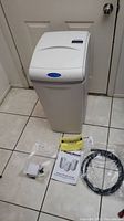 Front view of WaterBoss 900 water softener unit showing white plastic cabinet and label. Various accessories arranged in front including power adapter, tubing, and paperwork.