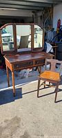 Front view of the antique vanity with tri-fold mirror and chair, showing surface wear and aged wood.