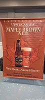 Front side of two-sided vinyl beer sign for Upper Canada Maple Brown Ale, showing bottle, glass, maple leaf and promotional text