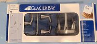 Box showing Glacier Bay brushed nickel bathroom set with faucet and accessories visible through plastic window.