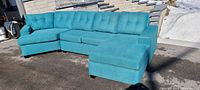 Blue sectional couch outdoors, full side and angle view showing entire 3-piece couch including chaise and ottoman.