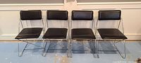 Front view of four chrome dining chairs with black padded seats and backrests, arranged in a row.