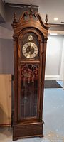 Front view showing entire wooden longcase clock with arched bonnet and finials