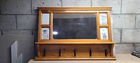 Front view of pine wood hall mirror showing central rectangular mirror, four photo frames, and five black coat hooks at bottom.