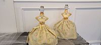 Front view of both vintage table lamps with female figurine bases wearing floral skirts, showing the lamp bulb holders.