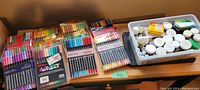 Full lot on table showing 11 sets of pastel markers and a plastic bin with inks and glitters
