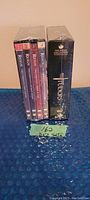 Side view of 8 DVD cases including 4 seasons of The Reign and a black collector's box of The Tudors, all sealed in plastic.