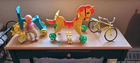 Wide shot of all vintage toys including Kewpie doll, wooden rocking horse, yellow bicycle model, and smaller toy pieces on wooden table