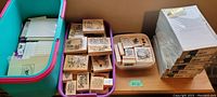 Image showing a large bin and a purple basket containing wood-mounted rubber stamps with visible floral and holiday designs alongside stacks of boxed stationery.